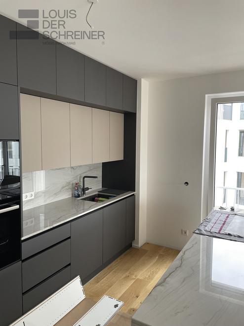 Eine maßgefertigte Küche mit mattschwarzen und beigen Fronten, eleganter Marmorarbeitsplatte und durchdachter Anordnung für optimale Raumnutzung und modernes Design.