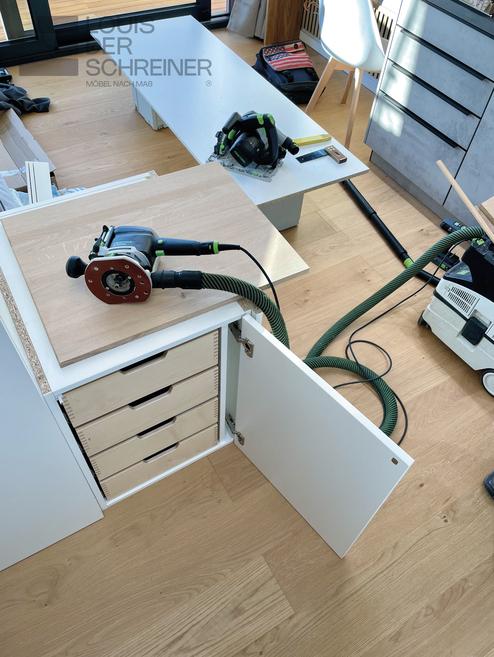 Eine maßgefertigte Schubladeneinheit während der Montage in einer Werkstatt. Verschiedene Holz- und Elektrowerkzeuge sind auf dem Werkstück platziert.