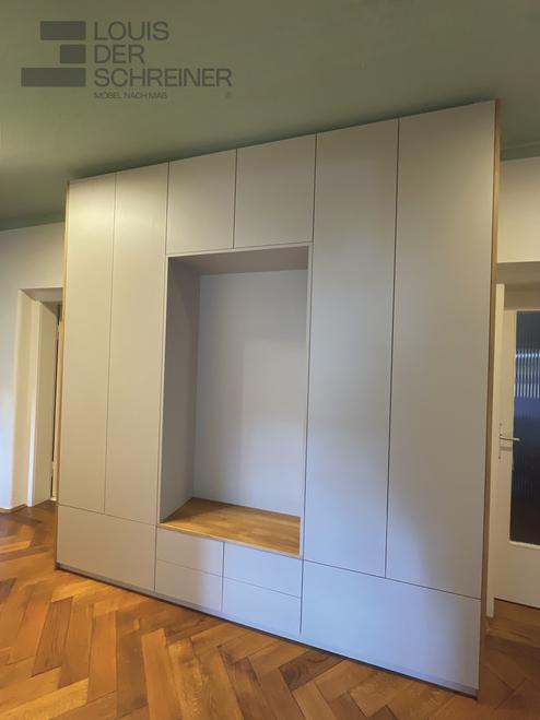 Eine hohe, maßgefertigte Schrankwand mit glatten Fronten und einer integrierten Holzsitznische.