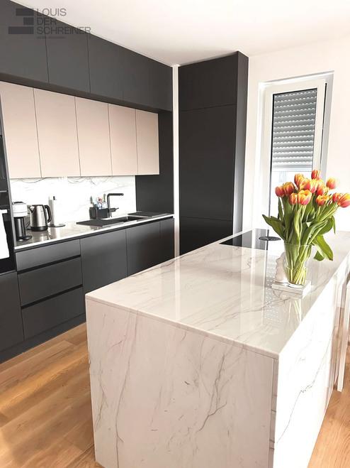 Maßgefertigte Küche in modernem Design mit dunklen Schränken und einer großen Kücheninsel aus weißem Marmor. Die Arbeitsplatte der Insel ist poliert und ein Strauß Tulpen sorgt für einen Farbakzent.