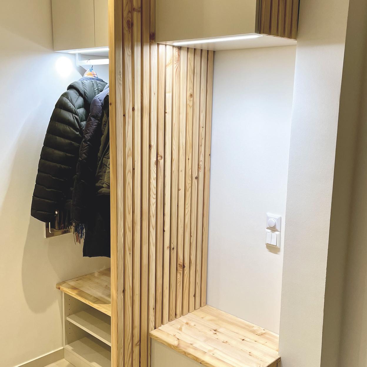 Garderobe nach Maß aus Holz und Weiß Maßgefertigte Garderobe mit Holzlamellen und integrierter Sitzbank in einer Nische. Die Garderobe bietet Haken und Ablageflächen für Jacken.