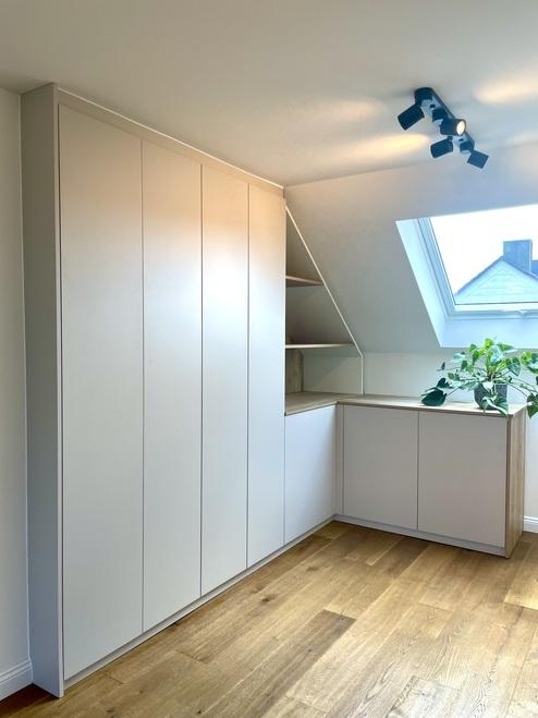 Maßgefertigter Dachschrägenschrank in schlichtem Weiß, integriert unter einer Dachschräge mit offenem Fach und dekorativer Pflanze.