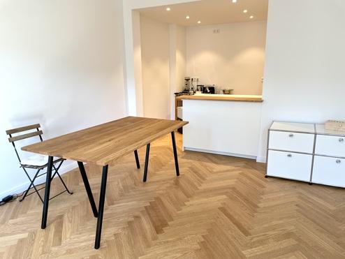 Hölzerner Tisch mit schwarzen Beinen, passender Stuhl und weiße Schrankmöbel nach Maß in einem hellen Raum.