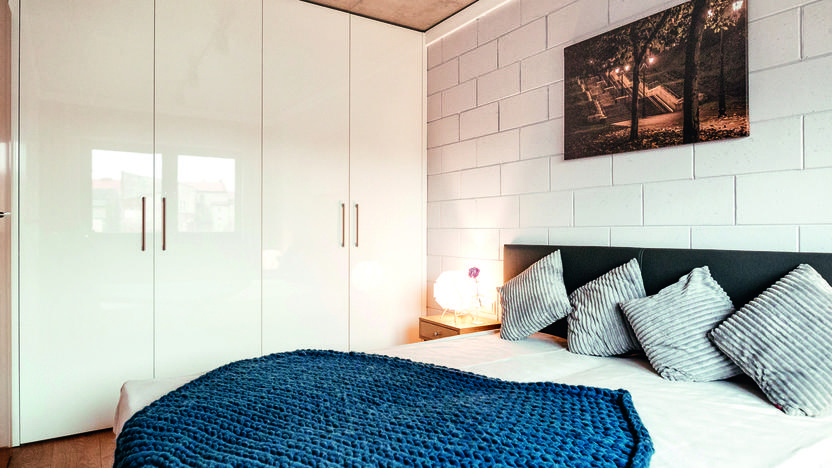 Modernes Schlafzimmer mit einem Bett, gestreiften Kissen und einer blauen Decke, sowie einem Bild an der Wand.