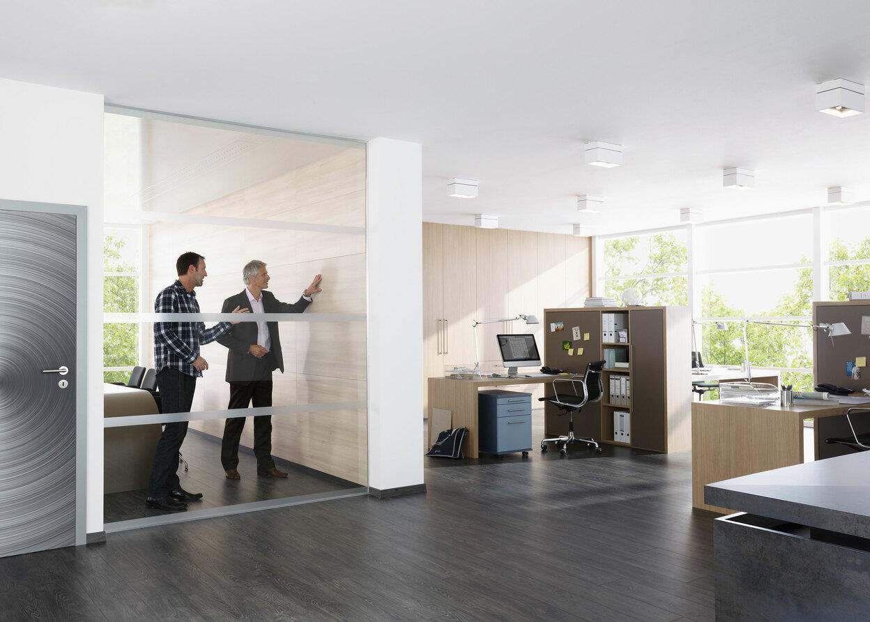 Impression eines Büros mit abgeschlossenem Raum mit Glaswand und offener Bürogestaltung.