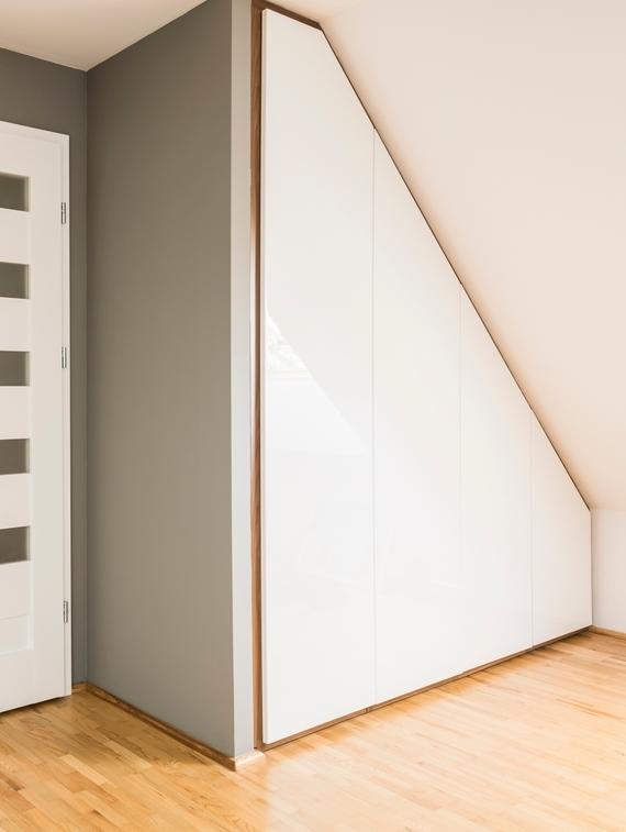 Weißer Einbauschrank an Dachschräge, dreieckig mit Trennwand zur Zimmertür an hellem Parkett.