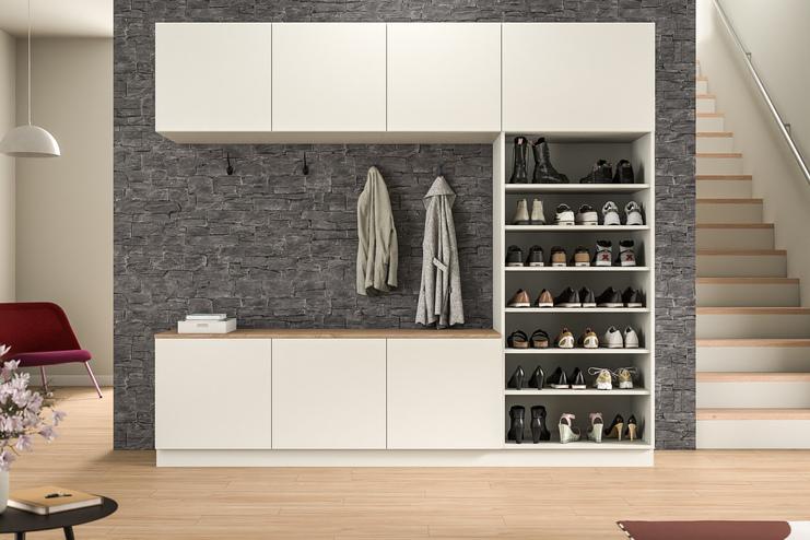 Maßgefertigter Schrankwand mit integrierter Garderobe im Eingangsbereich. Eine stilvolle Schrankwand nach Maß in weißer Farbe mit Schubfächern und einer offenen Nische für Jacken, vor einer markanten Steinwand, im Eingangsbereich.